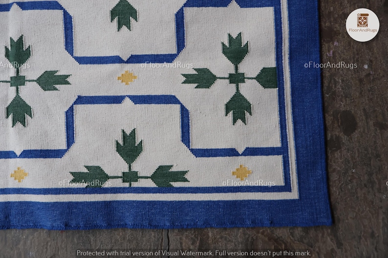 May include: A rectangular rug featuring a white background with a repeating geometric pattern in blue, dark green, and yellow. The design consists of blue linear borders framing dark green leaf-like motifs and small yellow diamond accents.