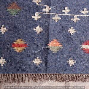 May include: A blue and white patterned rug with a fringe border. The rug has a geometric design with red, yellow, and green accents.