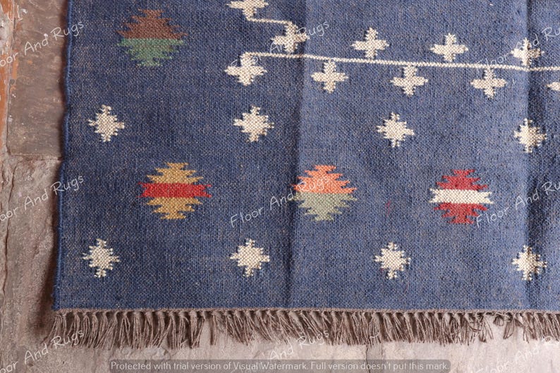 May include: A blue and white patterned rug with a fringe border. The rug has a geometric design with red, yellow, and green accents.