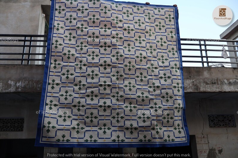 May include: A rectangular rug featuring a cream-colored base with a repeating grid pattern of dark blue lines. Within each grid square is a dark green floral motif and small yellow accents. The rug is finished with a solid dark blue border.