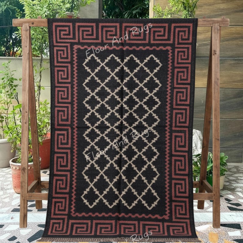 May include: A rectangular rug featuring a black background with a repeating beige diamond lattice pattern in the center. The border displays a continuous terracotta-colored Greek key design. The text Floor And Rugs is visible on the rug.