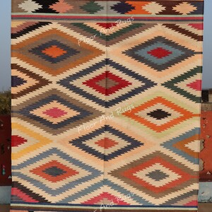 May include: A rectangular woven rug featuring a repeating geometric diamond pattern in shades of red, orange, blue, green, yellow, and brown. The rug has horizontal striped borders at the top and bottom with white fringe along the edges.