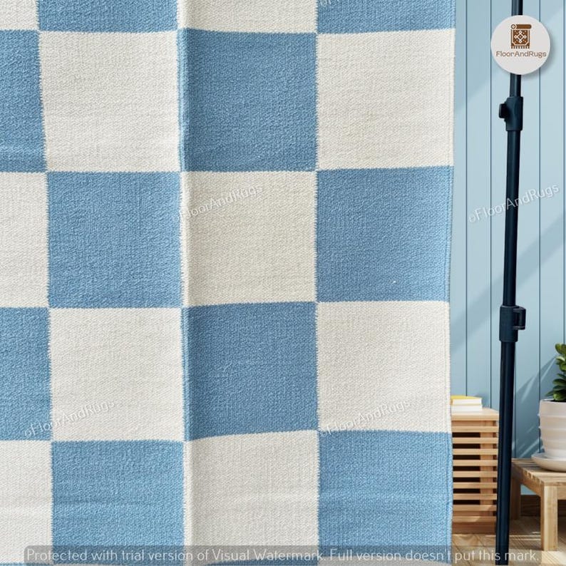 May include: A woven area rug featuring a repeating checkered pattern of light blue and off-white squares. The textile has a visible fabric texture and a consistent grid layout across the entire surface, creating a balanced geometric design.