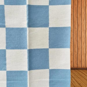 May include: A textile rug featuring a repeating checkerboard pattern of light blue and off-white squares. The fabric has a visible woven texture throughout the surface, with the watermark text FloorAndRugz appearing faintly across the design.