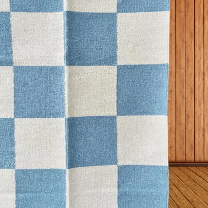 May include: A textile rug featuring a repeating checkerboard pattern of light blue and off-white squares. The fabric has a visible woven texture throughout the surface, with the watermark text FloorAndRugz appearing faintly across the design.