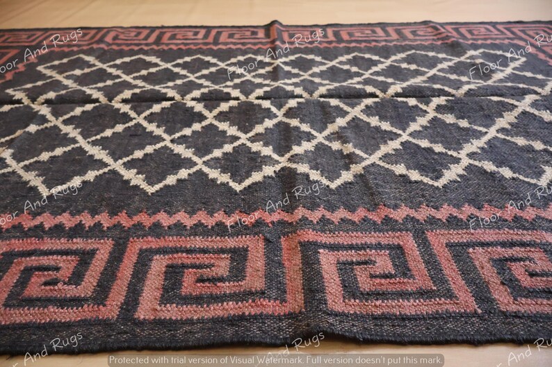 May include: A rectangular area rug featuring a dark charcoal background with a white diamond lattice pattern. The border displays a repeating pink Greek key motif separated by a zigzag line. The text Floor And Rugs is visible across the surface.