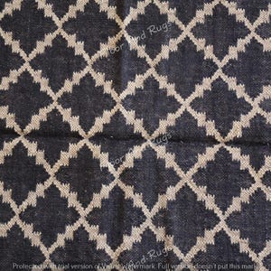 May include: A woven rug featuring a dark charcoal black base color with a repeating beige diamond lattice pattern. The textile surface displays a visible grid of intersecting lines that create a geometric design across the entire fabric area.