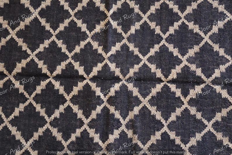 May include: A woven rug featuring a dark charcoal black base color with a repeating beige diamond lattice pattern. The textile surface displays a visible grid of intersecting lines that create a geometric design across the entire fabric area.