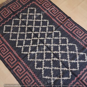May include: A rectangular area rug featuring a dark charcoal background with a central white diamond lattice pattern. The border displays a repeating pink Greek key motif. The rug has short fringe on the top and bottom edges.