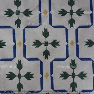 May include: A white textile featuring a repeating geometric pattern of blue interlocking lines forming octagonal shapes. Inside each shape is a dark green cross-like floral motif. Small yellow diamond accents are placed between the blue lines.