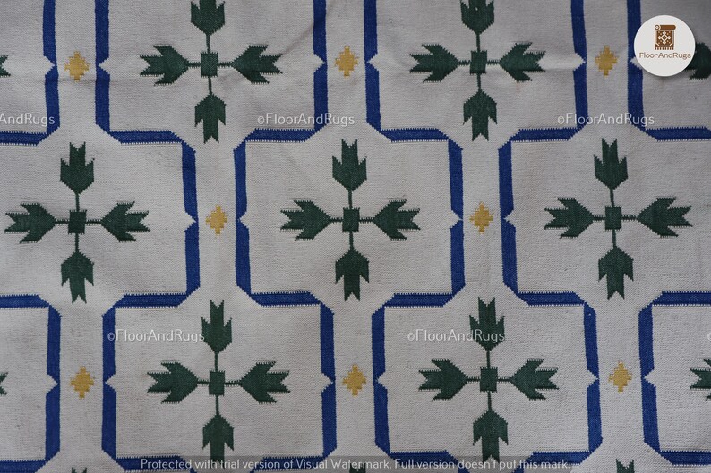May include: A white textile featuring a repeating geometric pattern of blue interlocking lines forming octagonal shapes. Inside each shape is a dark green cross-like floral motif. Small yellow diamond accents are placed between the blue lines.