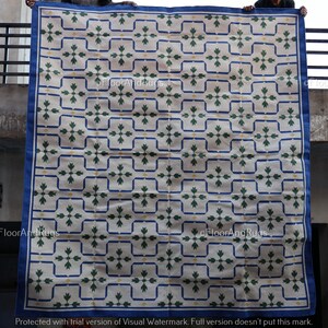 May include: A large rectangular area rug featuring a cream-colored background with a repeating grid pattern of dark blue lines. Each grid square contains a centered green floral motif with small yellow accents. The rug has a solid dark blue border.