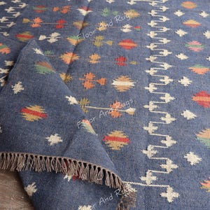 May include: A blue and white handwoven rug with a geometric pattern. The rug has a fringe border and is made of natural fibers.