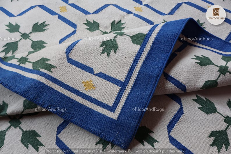 May include: A woven area rug featuring an off-white base with a repeating geometric pattern in blue, dark green, and yellow. The design includes blue outlined octagonal shapes, green leaf-like motifs, and small yellow cross-shaped accents.