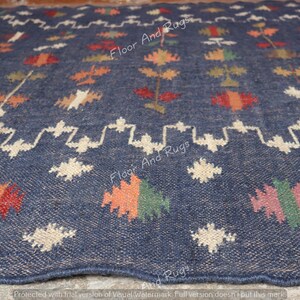 May include: A close-up of a blue rug with a white, orange, red, and green geometric pattern. The rug has a woven texture and is made of natural fibers.
