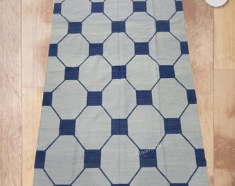 Puede incluir: Una alfombra rectangular con un patrón geométrico repetitivo de octágonos de color gris claro conectados por pequeños cuadrados de color azul oscuro. El diseño crea una cuadrícula estructurada en toda la superficie del revestimiento textil plano.