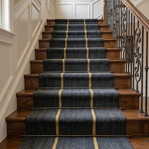 May include: A staircase featuring dark blue carpet runners with a single vertical gold stripe running down the center. The carpet is secured to the wooden steps with horizontal metal rods at the base of each riser, complemented by a black metal railing.