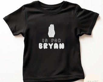 May include: Black t-shirt with a white graphic of a hand making the letter 'B' and the text 'IS FOR BRYAN'.