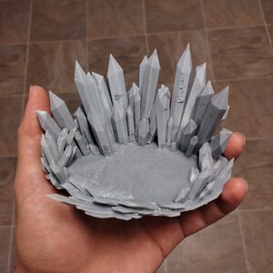 Può includere: Un modello di trono di cristallo stampato in 3D di colore grigio. Il trono è fatto di molti piccoli cristalli appuntiti che sono disposti in una forma circolare. Il trono ha un diametro di circa 15 cm e un'altezza di 10 cm.