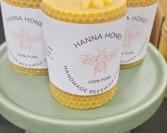 Puede incluir: Tres pequeñas velas de cera de abeja de color amarillo, con un patrón de panal, con etiquetas blancas. Las etiquetas presentan una ilustración de abeja y el texto "Hanna Honey" y "100% Cera de Abeja Pura Artesanal".