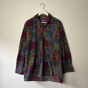 May include: A long-sleeved button-down shirt with a geometric pattern in shades of red, green, blue, and brown. The shirt is hanging on a white hanger. The label reads "Dante".