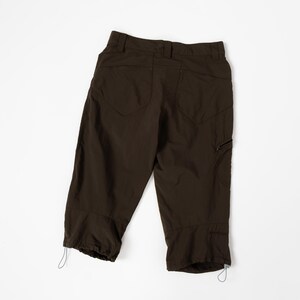 Puede incluir: Pantalones capri marr&oacute;n oscuro con dos bolsillos traseros, un bolsillo lateral con cremallera y ajustes con cord&oacute;n en el dobladillo. Los pantalones est&aacute;n hechos de un material ligero y se muestran sobre un fondo blanco.
