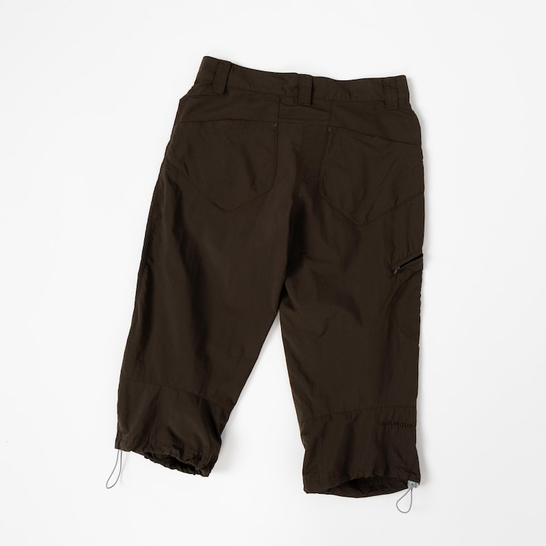 Puede incluir: Pantalones capri marr&oacute;n oscuro con dos bolsillos traseros, un bolsillo lateral con cremallera y ajustes con cord&oacute;n en el dobladillo. Los pantalones est&aacute;n hechos de un material ligero y se muestran sobre un fondo blanco.
