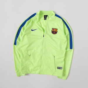 May include: A neon yellow long-sleeve track jacket with a full-length front zip, featuring a blue Nike swoosh logo on the right chest and the FC Barcelona club crest on the left chest, with blue stripes running down the length of each sleeve.