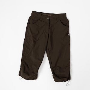 Puede incluir: Pantalones capri de color marr&oacute;n oscuro con m&uacute;ltiples bolsillos y cordones ajustables en el dobladillo. Los pantalones tienen cierre de bot&oacute;n y un dise&ntilde;o cl&aacute;sico de cinco bolsillos. La tela parece ser un material ligero y duradero.