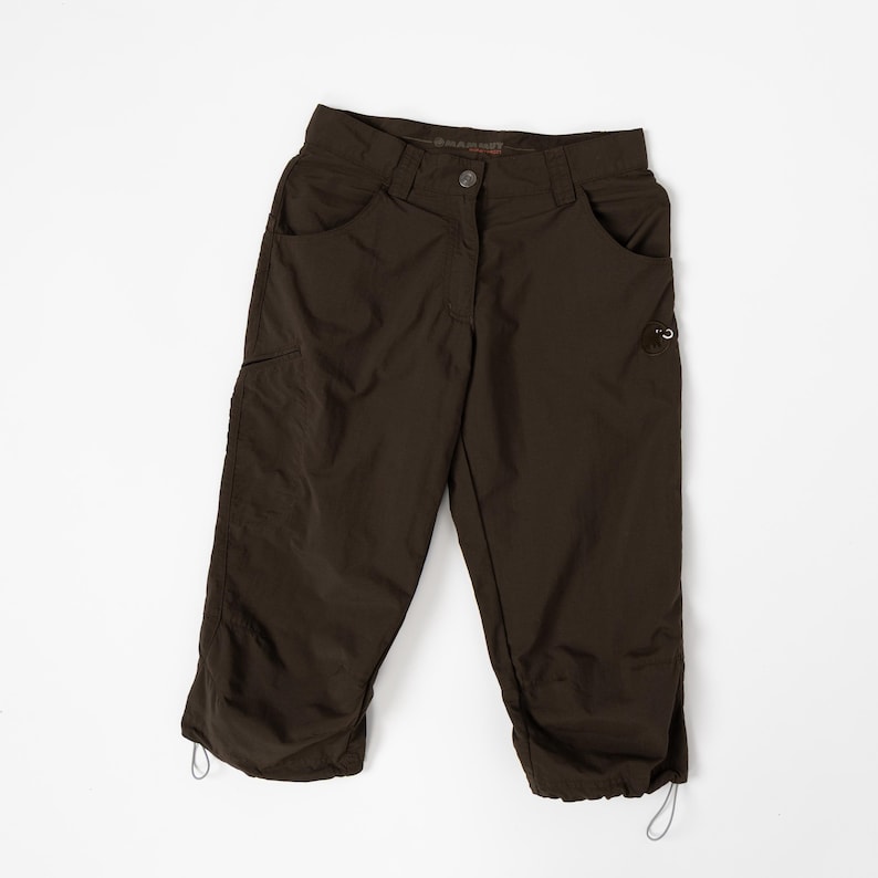 Puede incluir: Pantalones capri de color marr&oacute;n oscuro con m&uacute;ltiples bolsillos y cordones ajustables en el dobladillo. Los pantalones tienen cierre de bot&oacute;n y un dise&ntilde;o cl&aacute;sico de cinco bolsillos. La tela parece ser un material ligero y duradero.