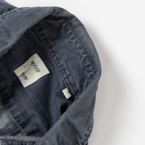 May include: A dark gray button-down shirt with a textured fabric finish. The interior collar features a white fabric label with the text Boggi Milano and Easy Formal Cotton Fit, along with a small white size tag displaying the letter S.