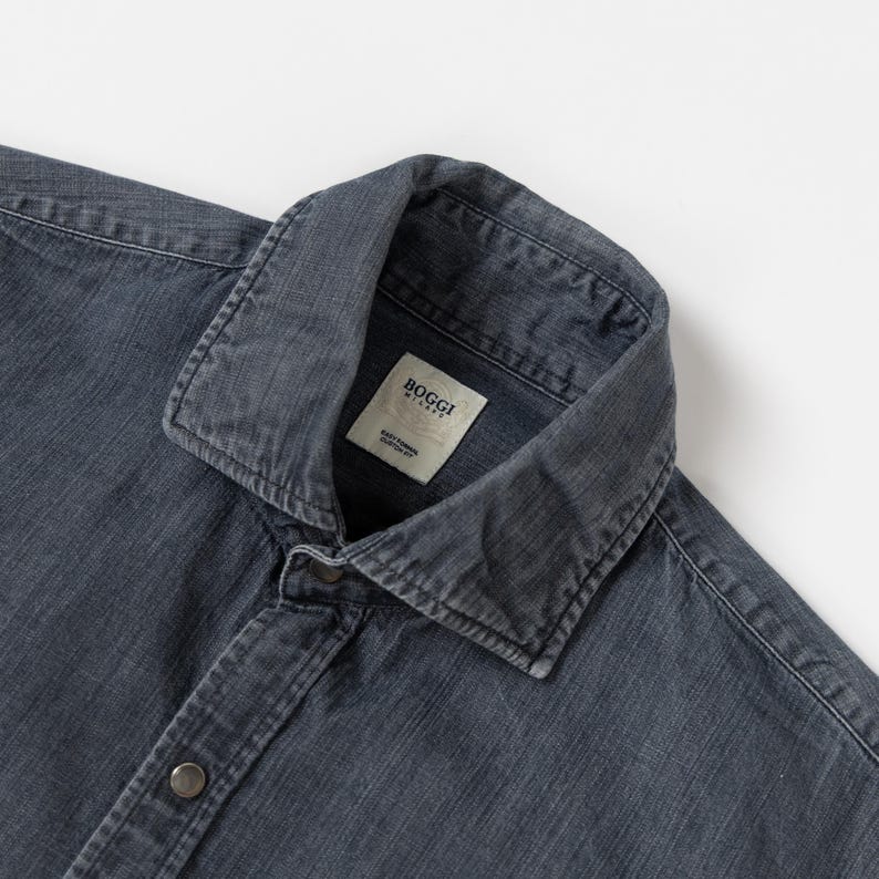 May include: A dark gray long-sleeve shirt with a spread collar and a button-down front. The shirt features a visible fabric texture and a white interior neck label that reads Boggi Milano Easy Formal Custom Fit in black text.