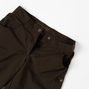 Puede incluir: Pantalones de exterior marr&oacute;n oscuro con cierre de bot&oacute;n y cremallera. Los pantalones tienen dos bolsillos delanteros y un peque&ntilde;o parche con el logotipo cerca del bolsillo derecho. La marca "Mammut" es visible en la cintura.