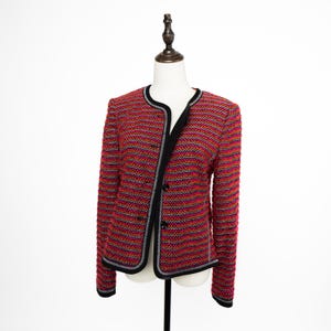 May include: A long-sleeved jacket featuring a textured, multi-colored knit pattern in shades of red, orange, and purple. The garment has a round neckline, a black trim along the front opening, and two black buttons for closure at the center front.