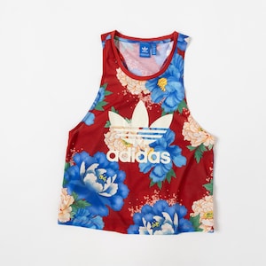 May include: A red sleeveless tank top featuring a large white Adidas trefoil logo and text on the front. The garment is decorated with a vibrant floral pattern consisting of large blue and pale yellow peony-like flowers and green leaves.