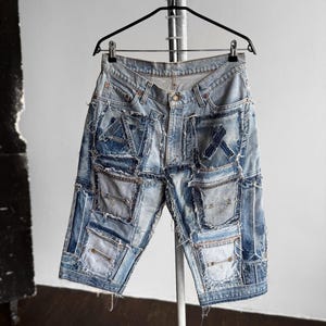May include: Light blue denim shorts with a patchwork design. The shorts feature multiple denim patches in varying shades of blue, creating a unique, distressed look. They are hanging on a black hanger against a white background.