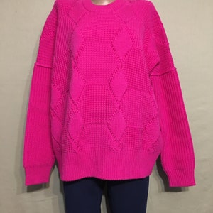 May include: A bright pink cable knit sweater with a loose fit and long sleeves.