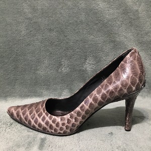 Op de afbeelding: Een enkele pump met een spitse neus. De schoen heeft een slangenprint in bruin- en grijstinten. De hak is ongeveer 7,6 cm hoog.