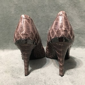 Op de afbeelding: Een paar pumps met een slangenpatroon in bruin- en grijstinten. De hakken zijn slank en de achterkant van de schoenen heeft een donker metalen accent.