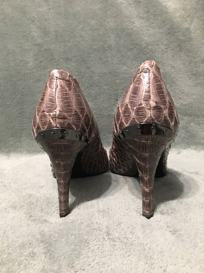 Op de afbeelding: Een paar pumps met een slangenpatroon in bruin- en grijstinten. De hakken zijn slank en de achterkant van de schoenen heeft een donker metalen accent.