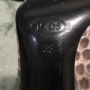Op de afbeelding: Close-up van de zool van een pumps. De zwarte zool is voorzien van het merk "TOD'S" en maat "38". De schoen heeft een slangenprint in grijstinten en beige. Maat 38.