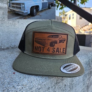 May include: A green and black trucker hat with a brown leather patch featuring a vintage pickup truck and the text "NOT 4 SALE". The hat has a black mesh back and a white "SNAPBACK" label.