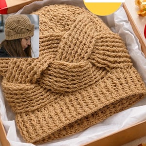 Puede incluir: Un gorro tejido a mano de color beige con un diseño texturizado, presentado en una caja de regalo. El gorro presenta un detalle trenzado único en la parte delantera. La imagen también incluye el texto "PDF+video".