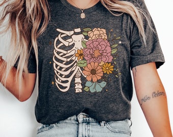 May include: A dark grey t-shirt with a floral design inside a ribcage. The flowers are pink, yellow, orange, and blue.