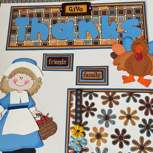 May include: A Thanksgiving scrapbook page with a blue and white pilgrim girl, a brown turkey, and a brown and blue patterned background. The page says "Give Thanks" and includes the words "friends" and "family".