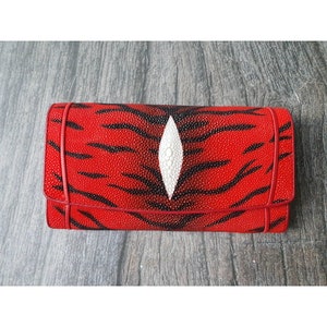 Puede incluir: Cartera roja con estampado de rayas de tigre negras y un diseño ovalado blanco en el centro. La cartera está hecha de un material texturizado y tiene un borde rojo.