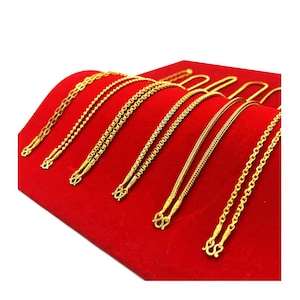 Puede incluir: Una colección de cadenas de oro de diferentes estilos y longitudes, expuestas sobre un fondo de terciopelo rojo.