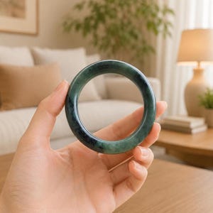 May include: A smooth, circular bangle bracelet crafted from dark green jade with natural mottled patterns and a polished, glossy finish. The bangle features a solid, continuous band design with a rounded profile and a deep, rich emerald hue.