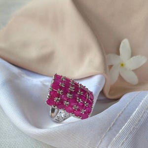 May include: A silver ring with a square-shaped setting filled with pink ruby stones.