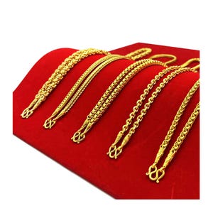 May include: Six gold chains of different styles and lengths displayed on a red velvet surface.